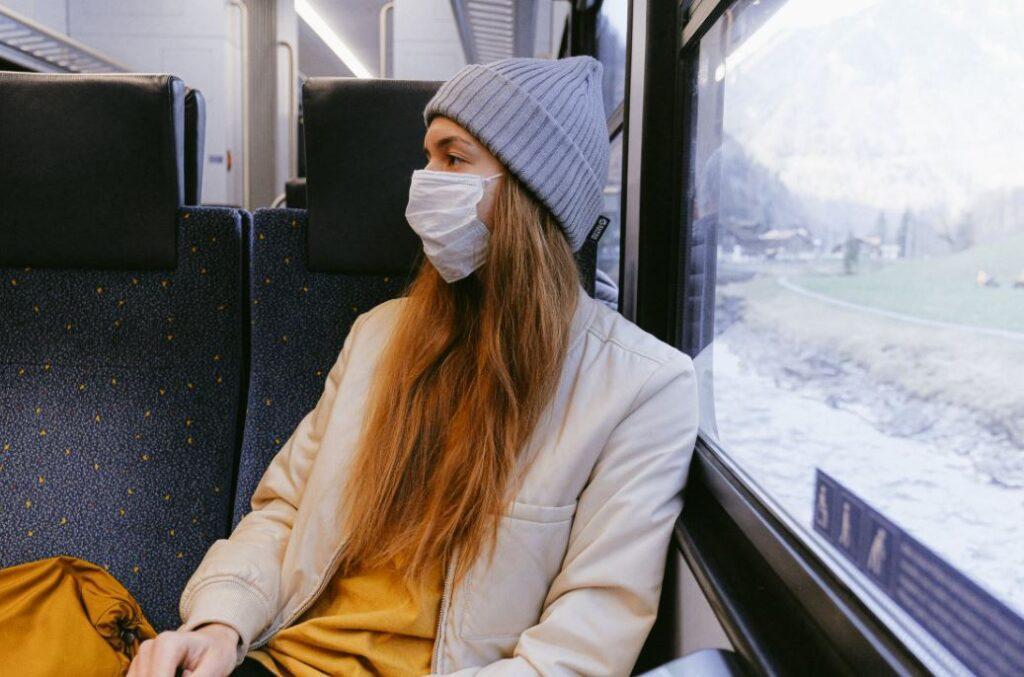 Frau sitzt mit Schutzmaske im Zug